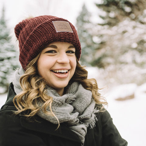 A smiling student in a maroon beanie and gray scarf enjoys a snowy outdoor setting
