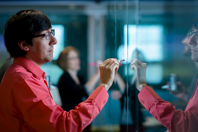 graduate student writes on a glass board during a discussion