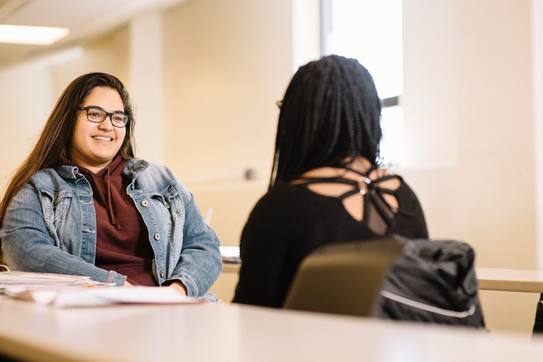 Student meeting one-on-one with a peer in a classroom setting.