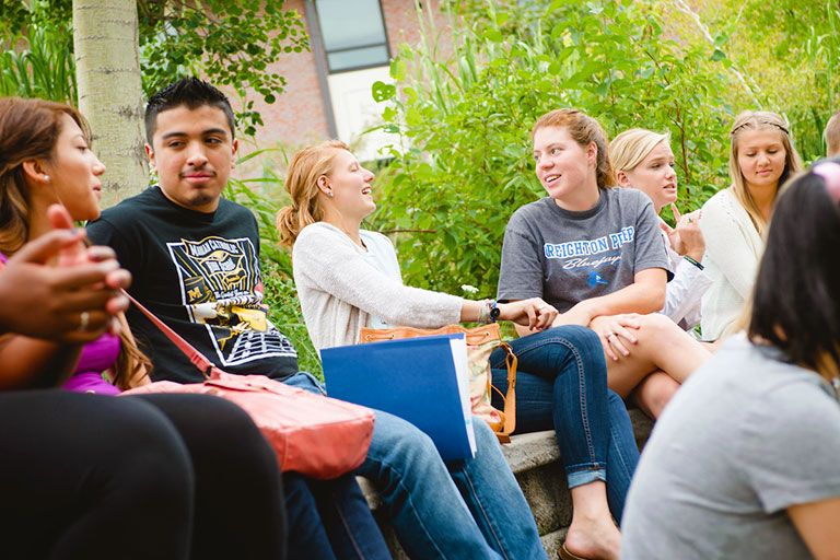 a group of students sits outside smiling and talking in pairs on the northwest Denver campus