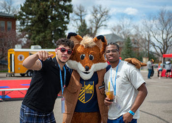 Mascot Regi the Fox poses with two students during Welcome Week on campus