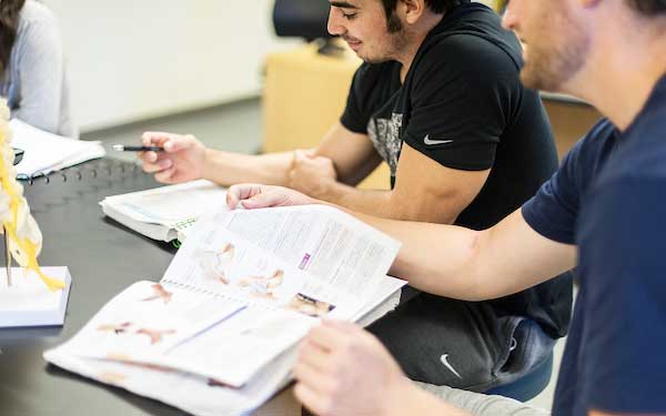 students sit at lab tables in a science classroom looking at textbooks and anatomical models