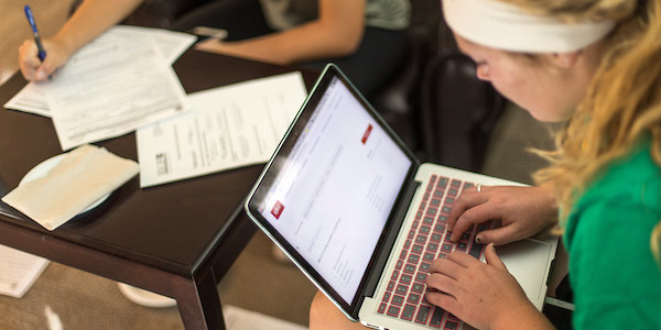 two students study with a laptop and pen and paper