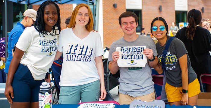 students in Regis gear pose for a photo under a tent at Welcome Week on the Quad