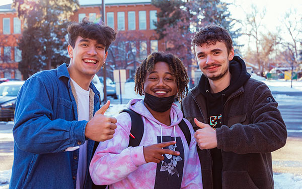 smiling student give thumbs up and peace signs on a snow-covered campus