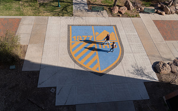 Two students walking over Regis shield near Desmet and O'Connell hall