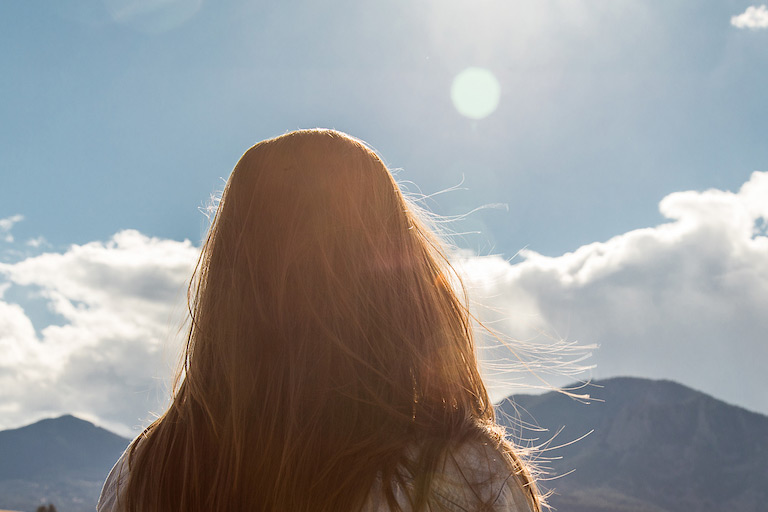 women seen from behind stands in front of mountains in the sun