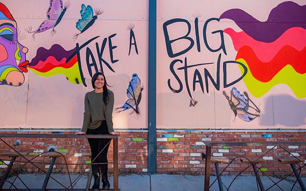 student standing in front of mural