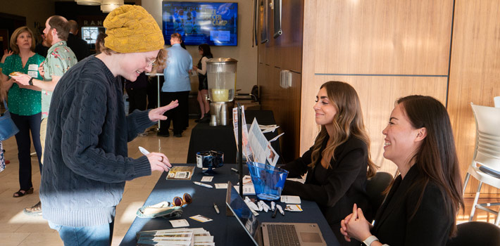 Table in the middle of the frame with a prospective student on the left and two Regis counselors on the right talking to each other