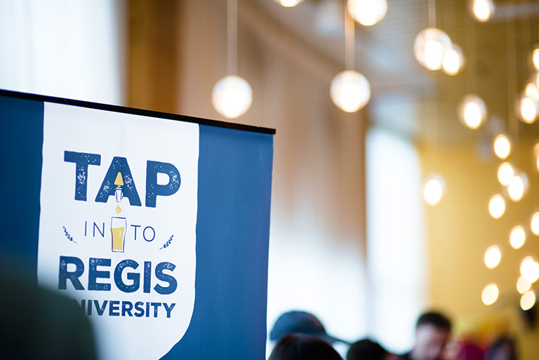 banner reading "Tap into Regis University" in a room with warm lights