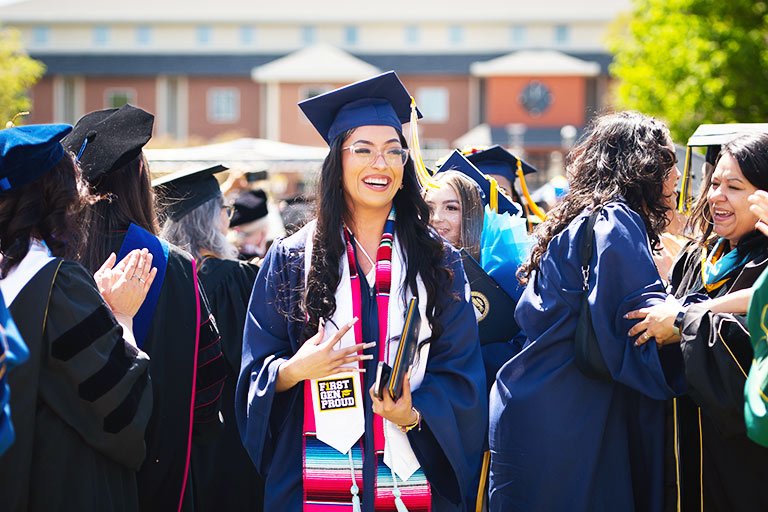 a graduate smiles as she leaves the commencement stage with her diploma on the Regis campus in Denver, Colorado
