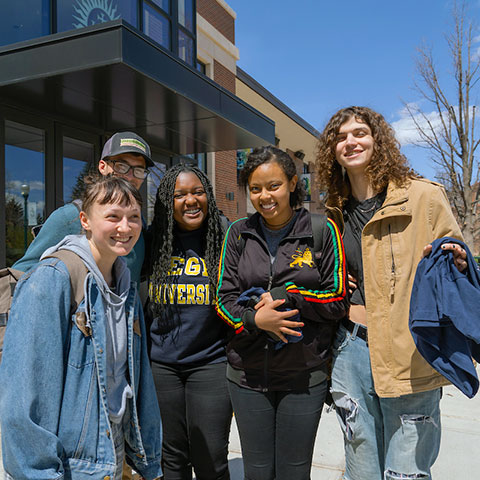 a small group of students smiles for a photo on the Quad outside the Student Center