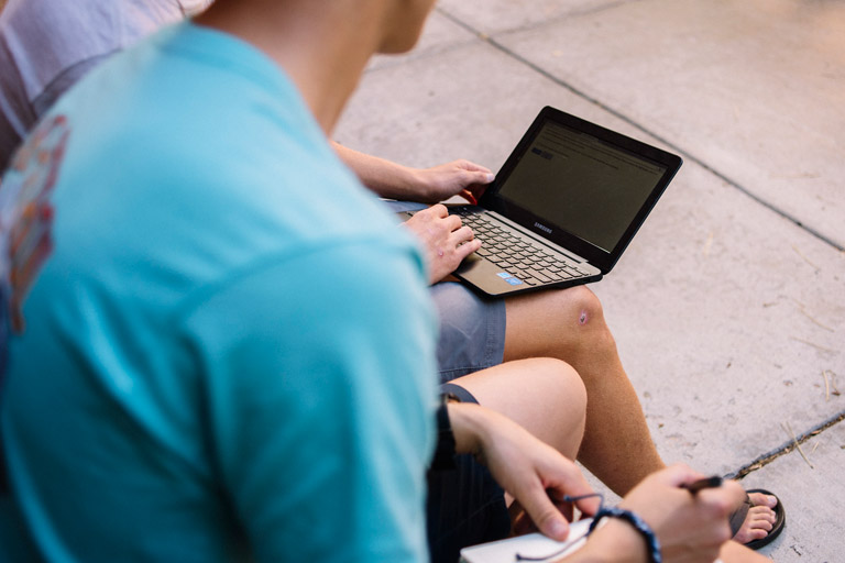 computer and notebook on knees of students outside