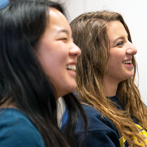 two students sit side-by-side smiling