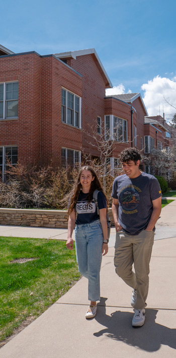 Two students conversing and walking through the sidewalks of Residence Village on Regis Northwest campus