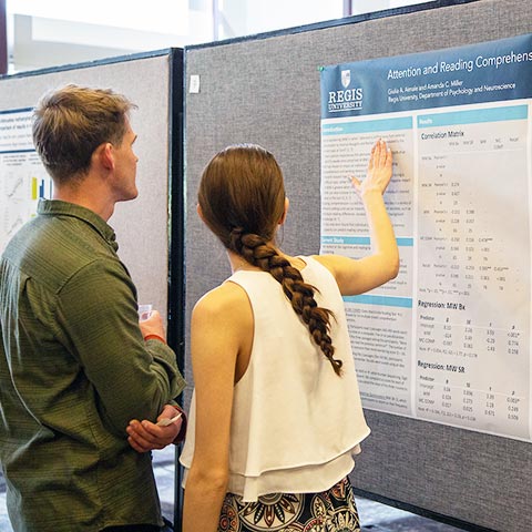 a man and a woman look intently at a poster titled Attention and Reading Comprehension at the URSC Research Fair in the Mountain View Room on the Northwest Denver campus