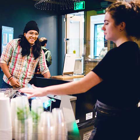a student stands at the counter ordering while a student worker gets his order ready in Walker's Pub on the Northwest Denver campus