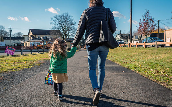 a woman and a child hold hands and walk down a trail