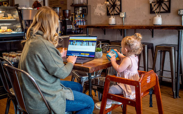 young woman works on laptop while tending her baby and sitting in a coffee shop