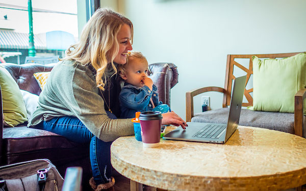young woman works on a laptop with a toddler in her lap