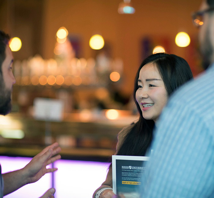 woman smiles while talking with admissions counselors at a Tap into Regis event