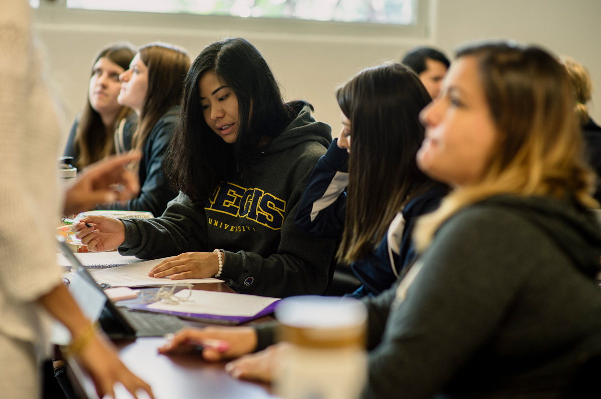 students seated in classroom, reviewing notes and engaging in conversation