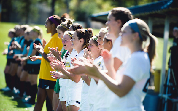 women's soccer players cheer from the sidelines