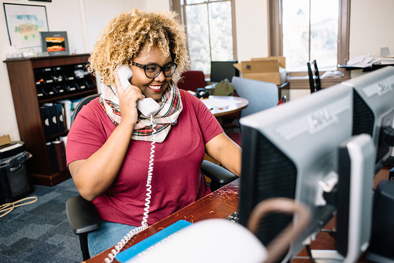 Young woman talks on the phone while seated at a computer in an office