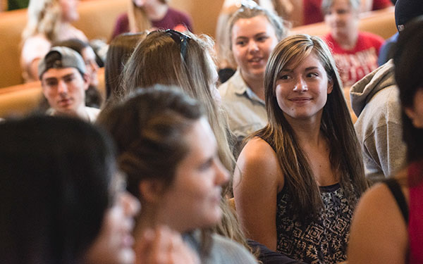 young woman sits in a crowd and smiles