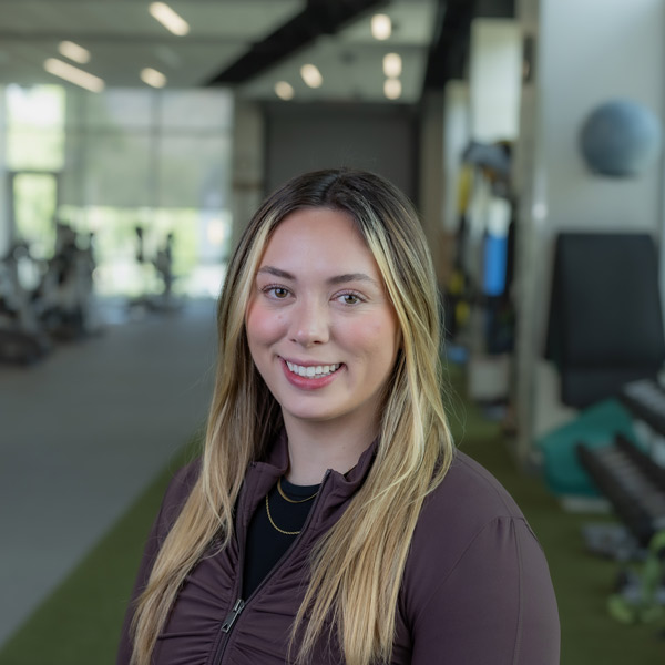 Riley Tara, stands in a gym with equipment behind