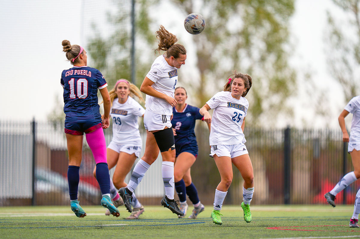 Madison Cullinan heads the ball while teammates and opponents look on during a game on the Regis match pitch