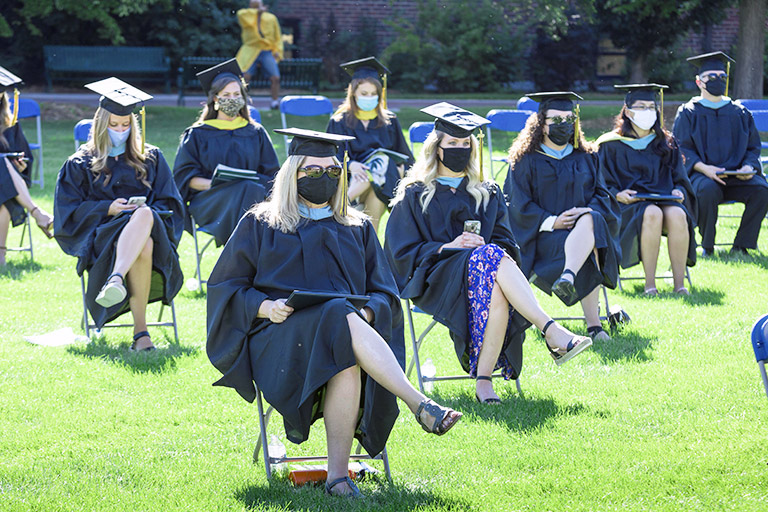 graduates sit in socially distanced rows wearing masks at the 2020 commencement ceremony on the Regis quad