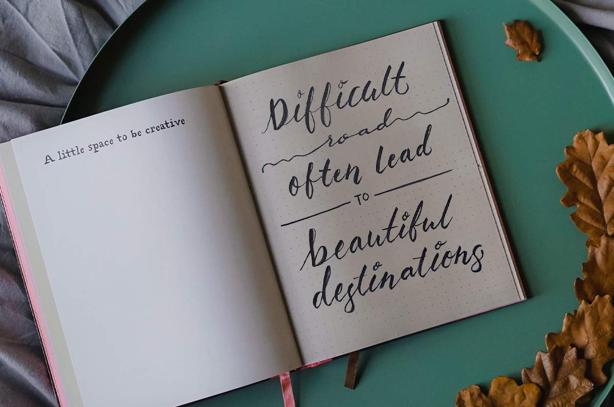 Open notebook with handwritten quote: "Difficult roads often lead to beautiful destinations"