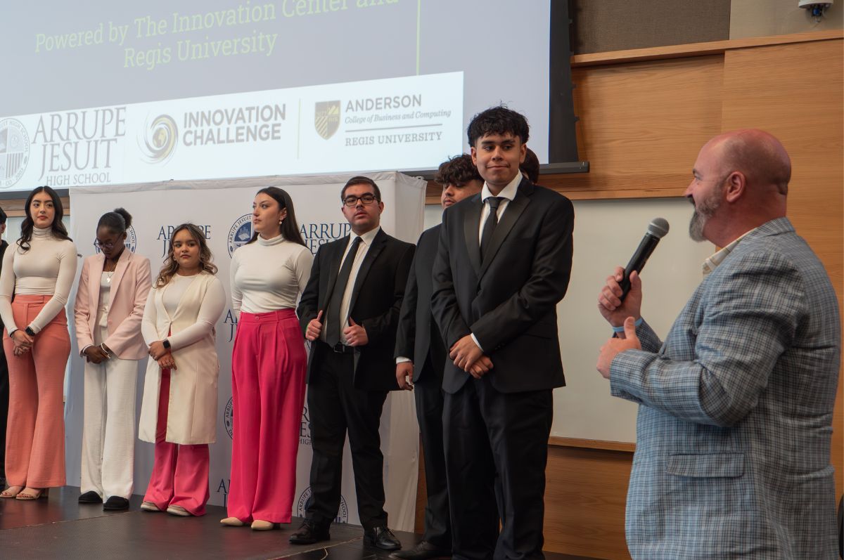 students stand on stage as professor speaks to them