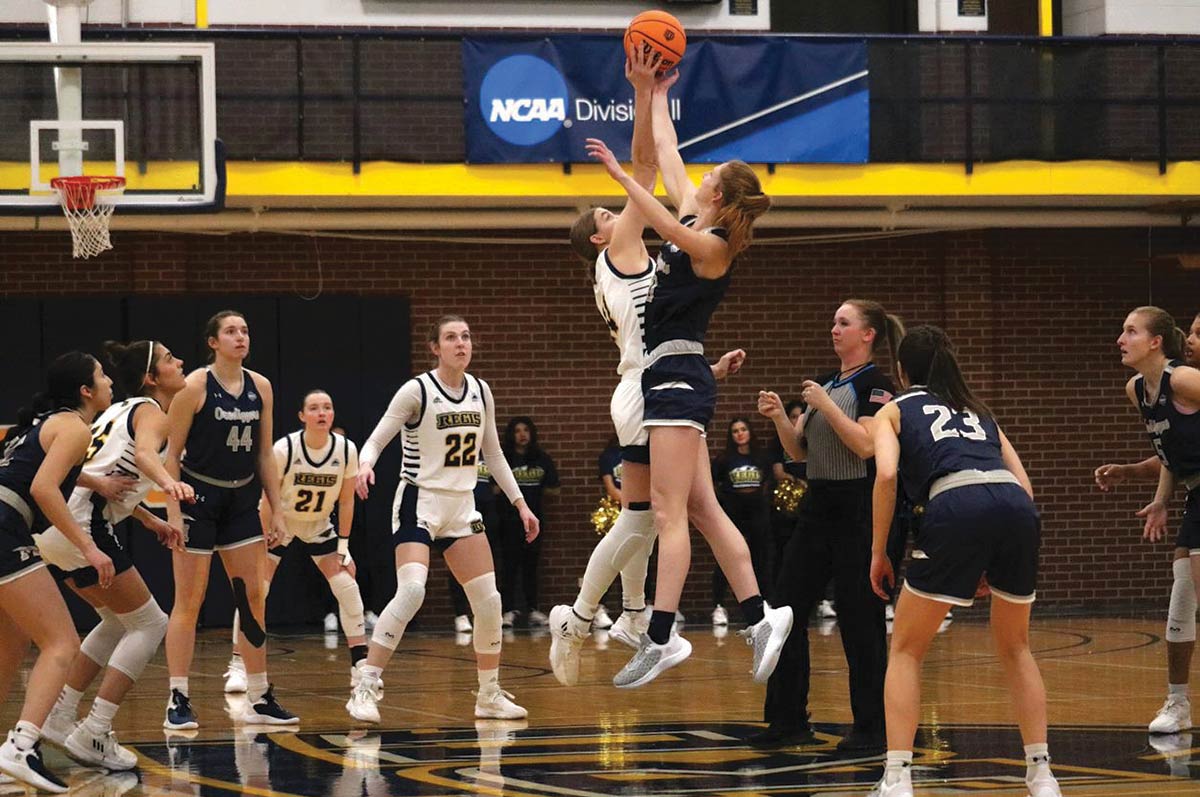 A Regis player and opponent jump for the tipoff ball while their teammates look on, poised for action, in the Regis University Fieldhouse on the Northwest Denver campus.