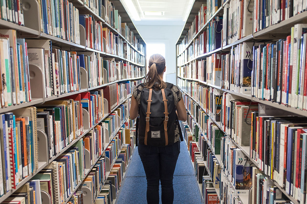 Student walks through book shelves in Regis University's Dayton Memorial Library