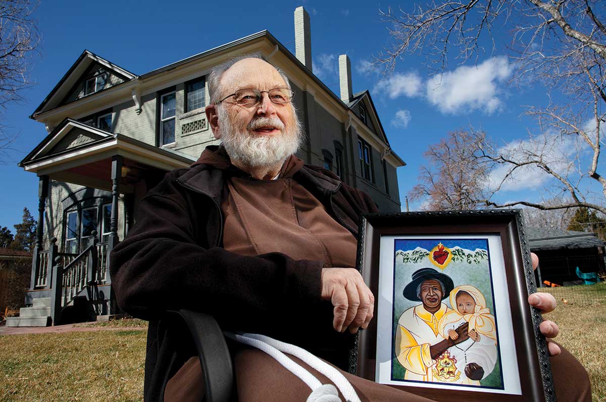 Rev. Blaine Burkey sits outside holding the Archodiocese’s painting of Greeley.
