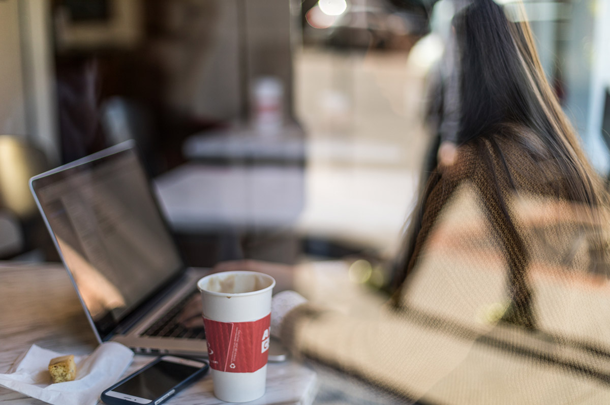 woman on computer in cafe, reflection of man walking