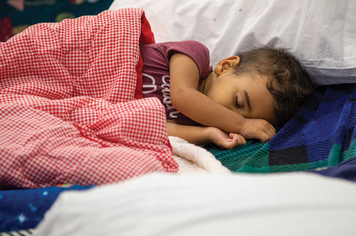 A small child sleeps peacefully among blankets and pillows at the Regis Welcome Center.