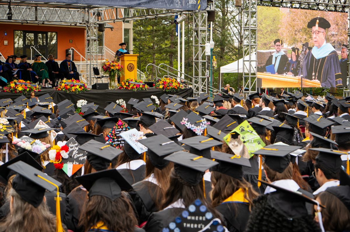 graduates listen to President Salvador Aceves speak on stage