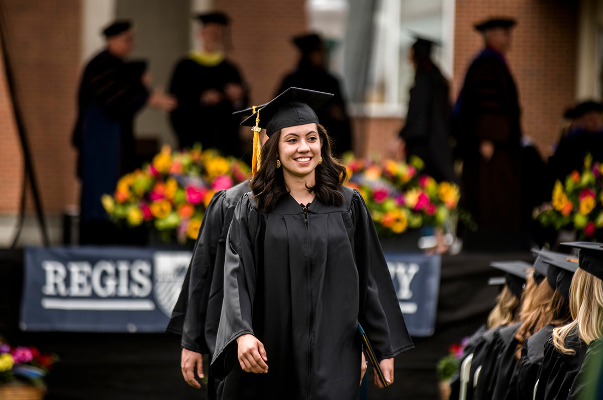 a graduate wearing regalia smiles as she walks down the aisle after receiving her diploma on stage at the commencement ceremony on the Northwest Denver campus