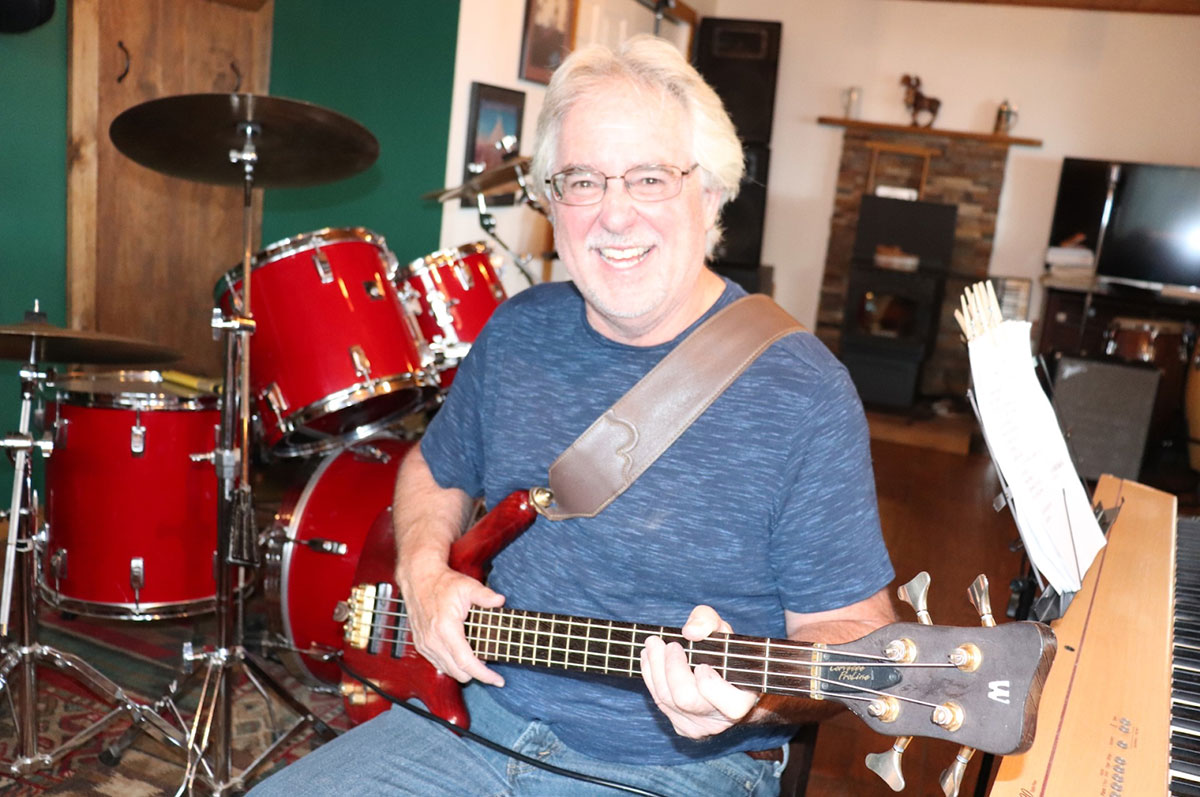 Don Bush sits in a music studio near a drum set and keyboard holding an electric guitar