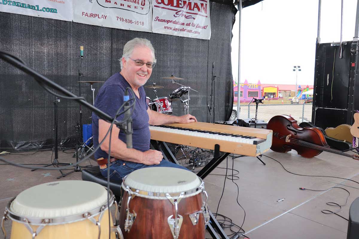 Don Bush sits behind a keyboard while performing on stage with a band