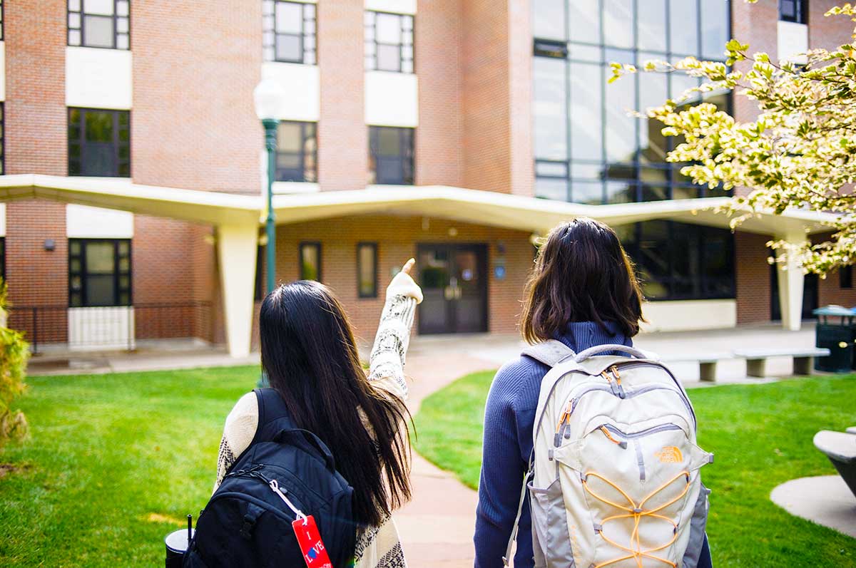 students walk outside wearing backpacks outside Carroll Hall on the Northwest Denver campus