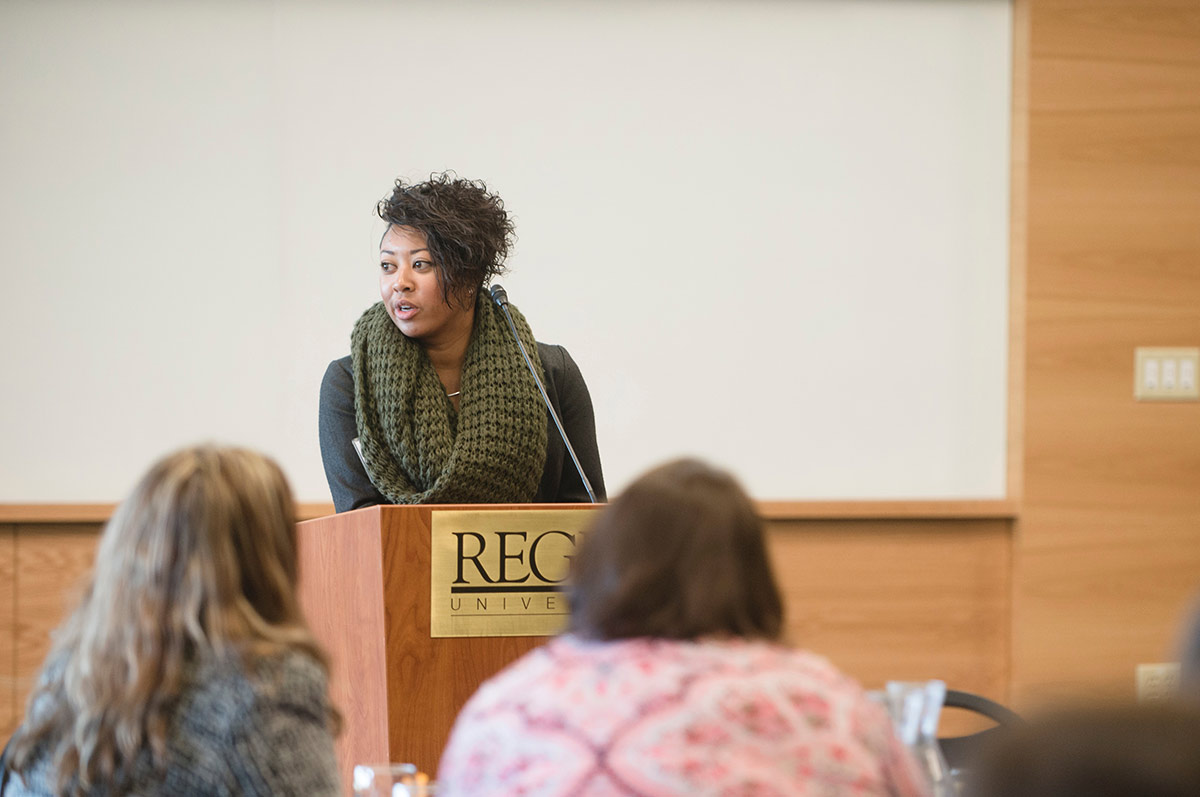 a woman stands, speaking at a podium of an audience  in the Mountain View Room on the Northwest Denver campus