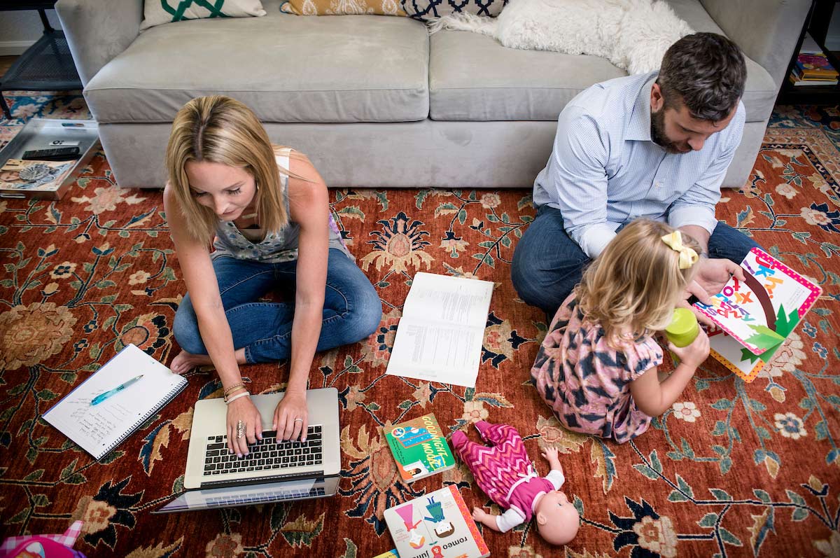 woman works on laptop while man and small child look at book