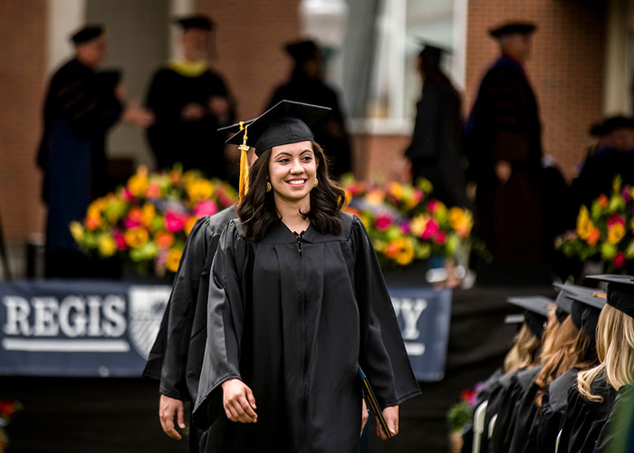 smiling graduate wearing regalia walks down the aisle at commencement on the Northwest Denver campus