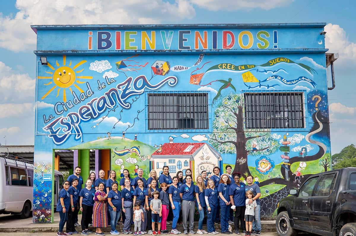 a group of students and workers pose for a group shot outside La Ciudad de La Esperanza in Coban