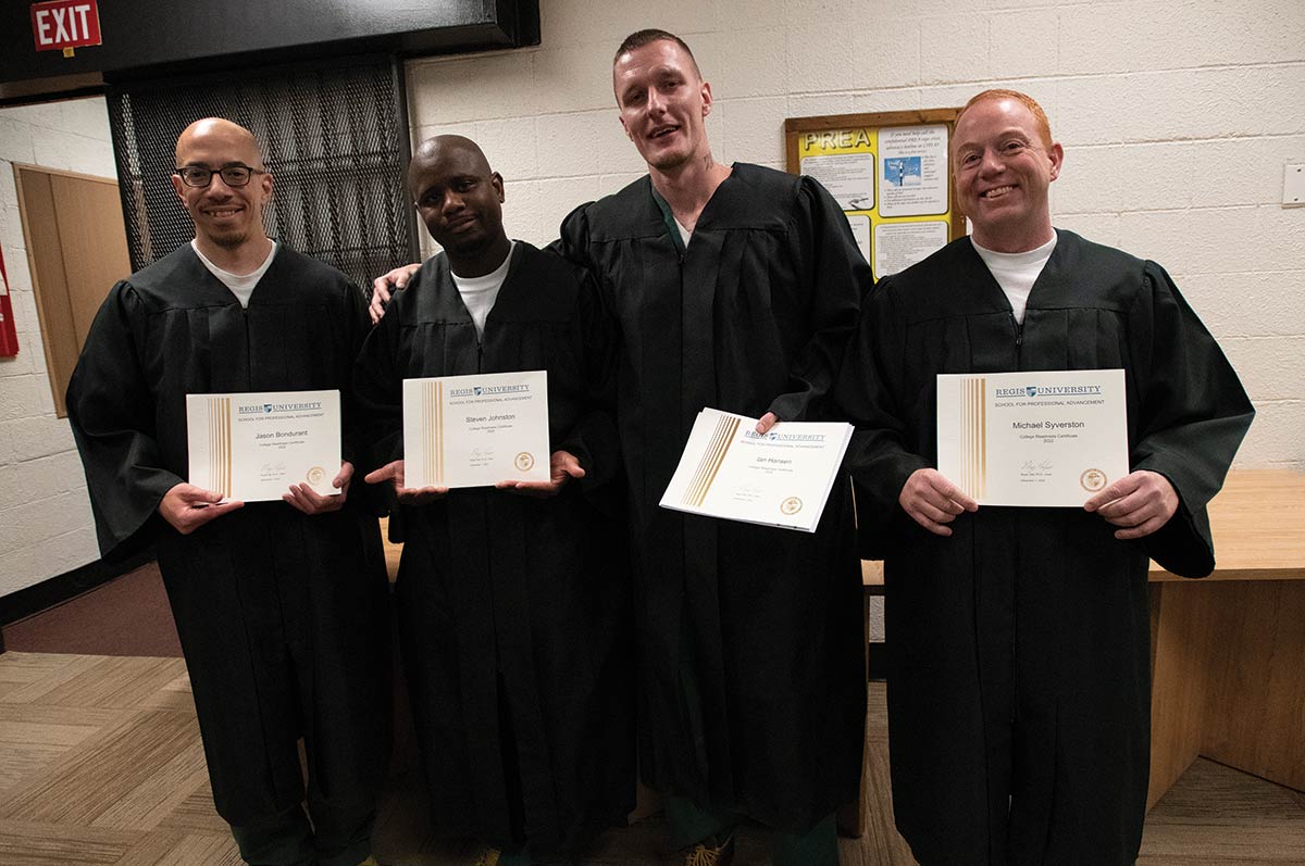Four Inside/Out graduates wear graduate robes and proudly display their certificates of completion.