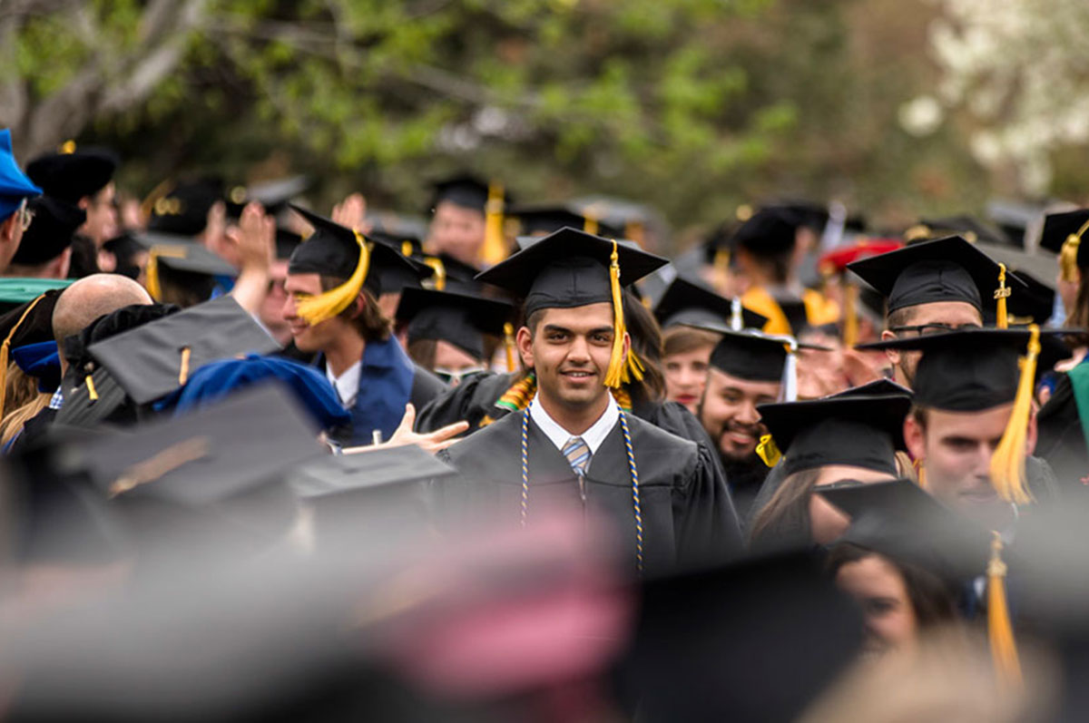 Male graduate stands smiling in crowd at commencement